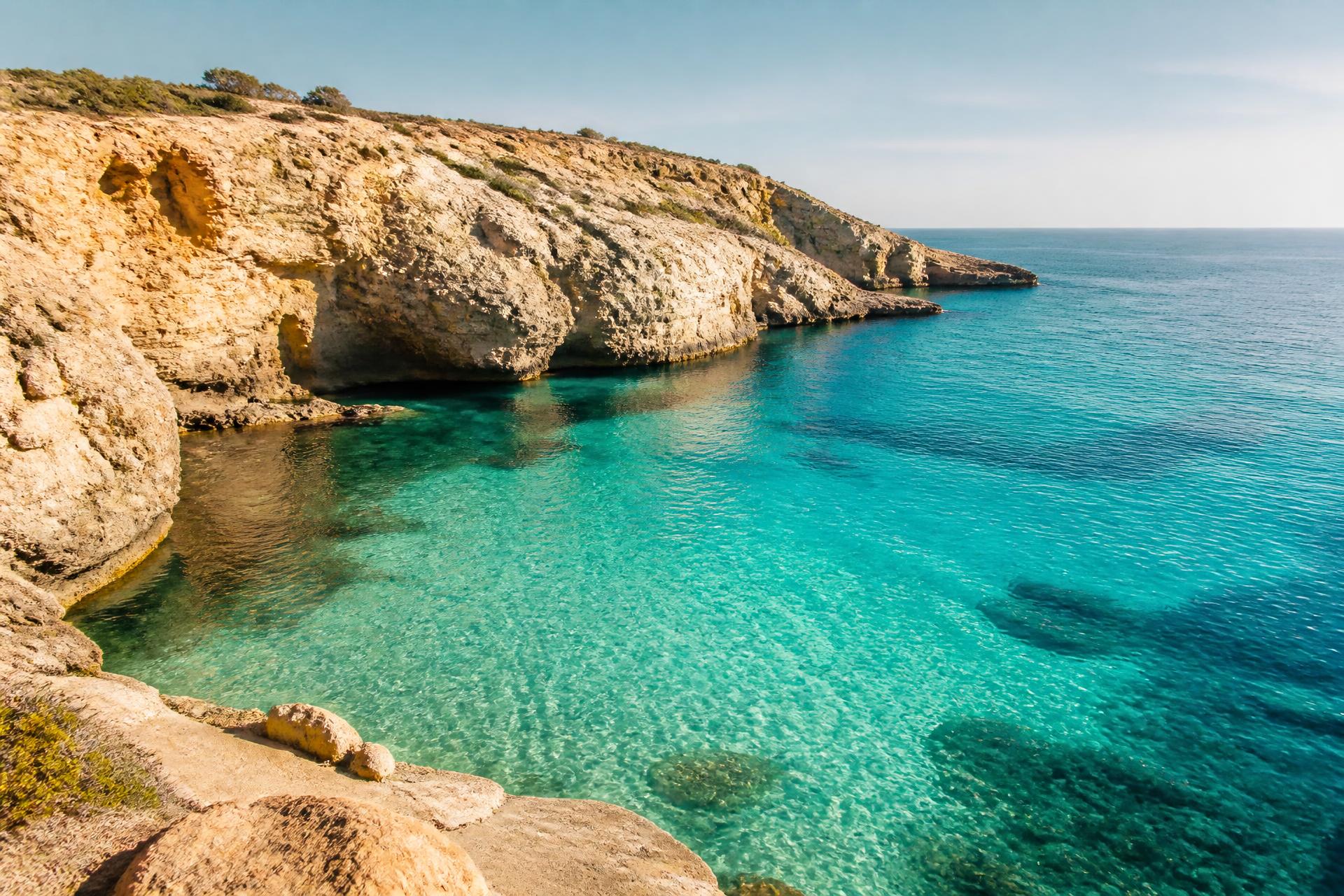 Turquoise cove beneath golden limestone cliffs on a southern European coast